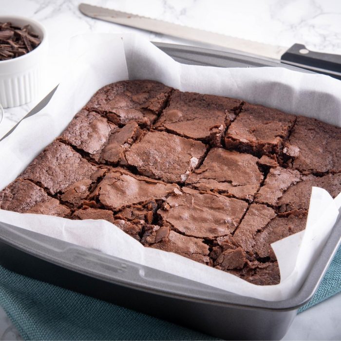 A tray of baked Chocolate Brownies in a square brownie baking tin.