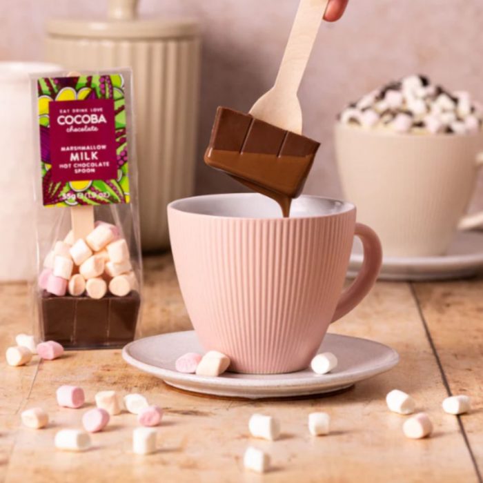 hot chocolate stirrer melting into a pink mug of hot milk and marshmallows scattered around.