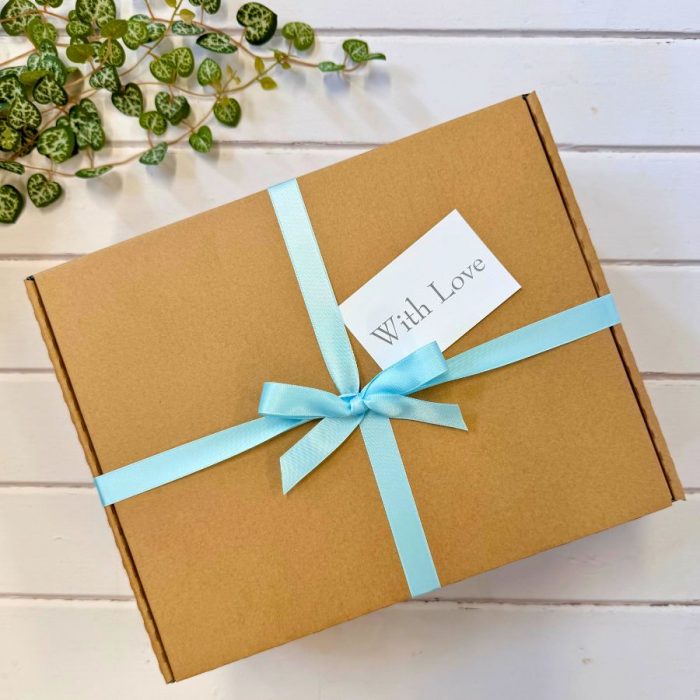 A hamper gift box with pale blue ribbon, with love gift tag and folliage in the background.
