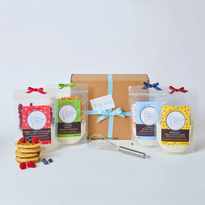 4 gourmet pancake mixes, a metal whisk and a stack of pancakes in front of the Pancake Hamper Box