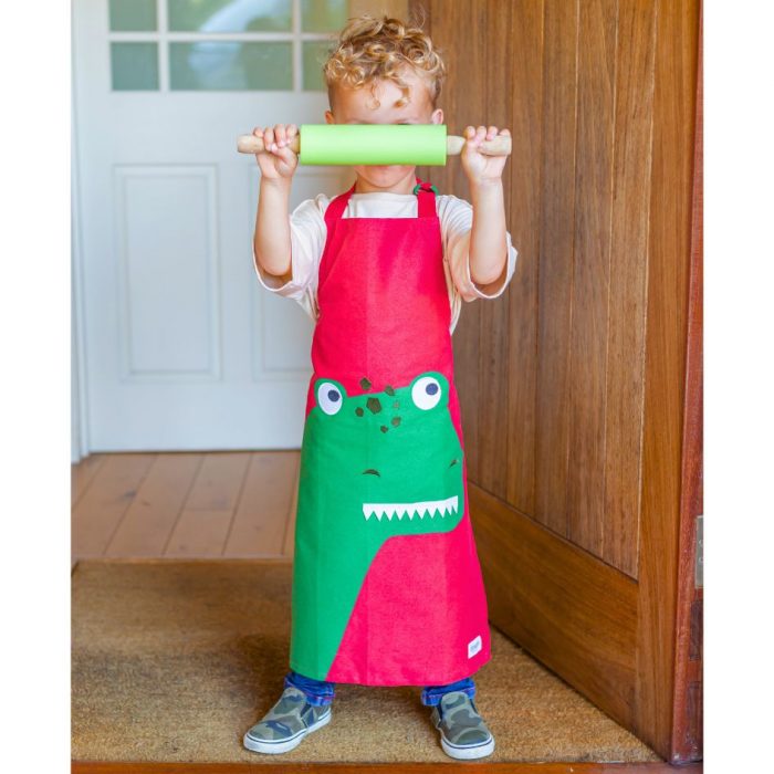 child wearing a red and green dinosaur apron and holding a rolling pin